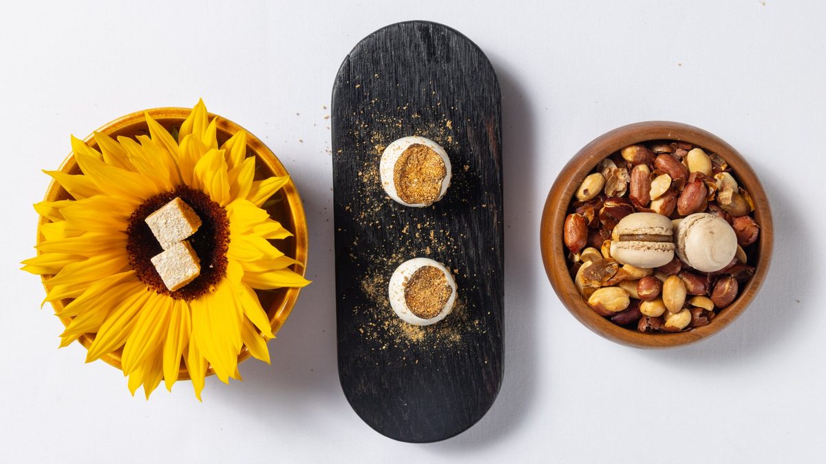 Petit fours van Salsify at the Roundhouse in Kaapstad, bedien op ’n sonneblom, ’n swart houtbord en in ’n houtbak met grondboontjies